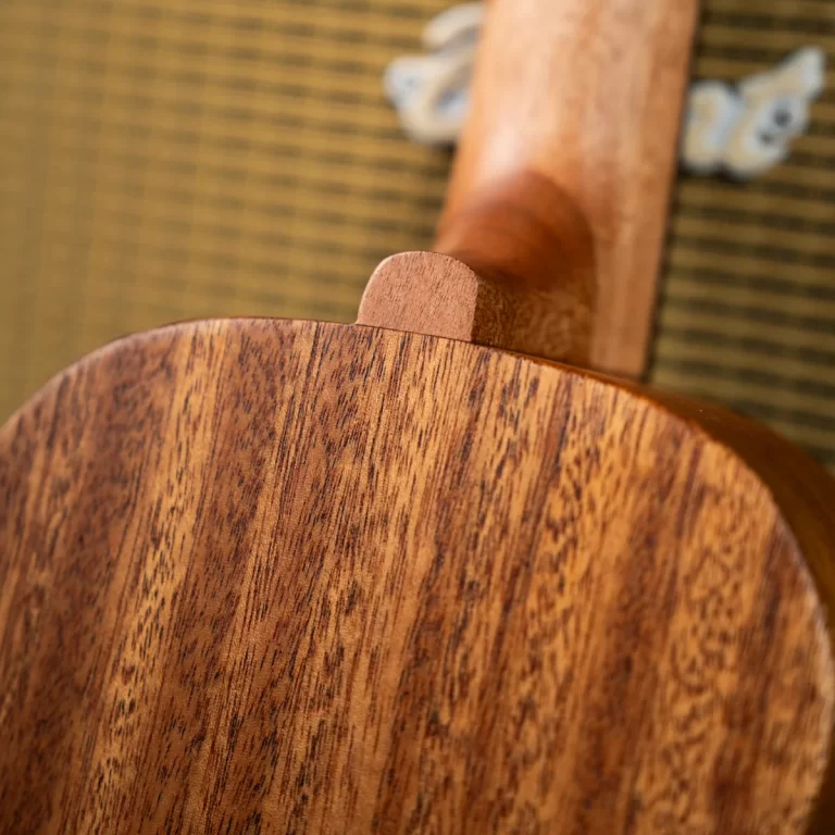Close-up of a wooden guitar neck joint where the neck meets the body, showing rich wood grain and a rounded joint edge. ขายราคาพิเศษ