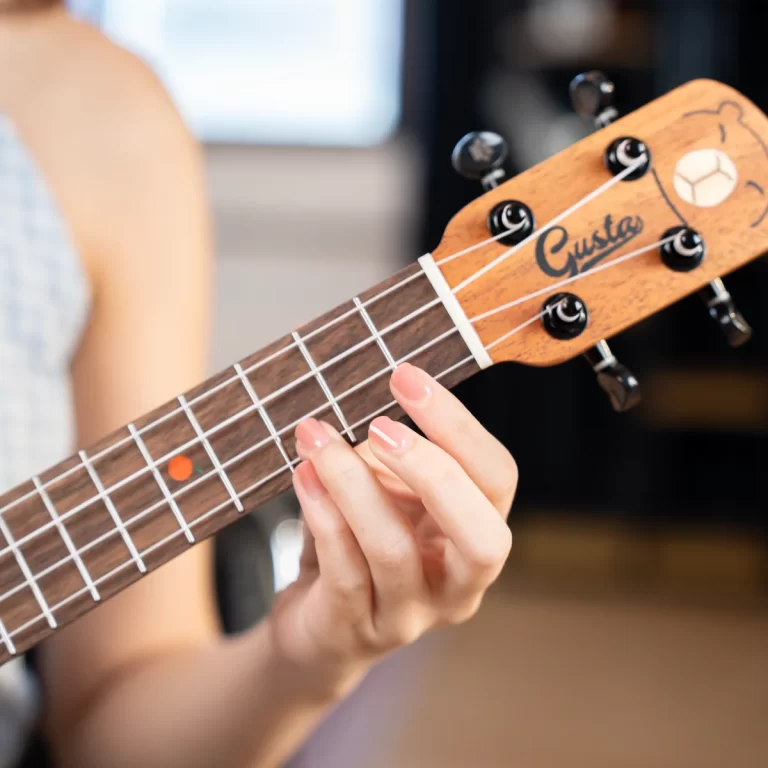 Close-up of a hand pressing frets on a wooden ukulele neck, headstock with tuning pegs in view. ขายราคาพิเศษ