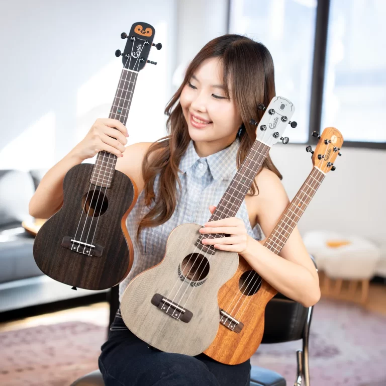 Smiling woman sitting indoors, holding three ukuleles of different finishes on each arm and lap? Actually not necessary; I will write better. ขายราคาพิเศษ