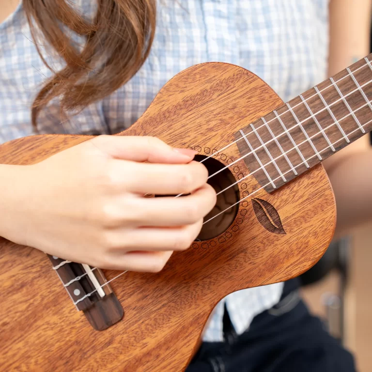 Close-up of a person strumming a wooden ukulele, focusing on the strings and sound hole. ขายราคาพิเศษ
