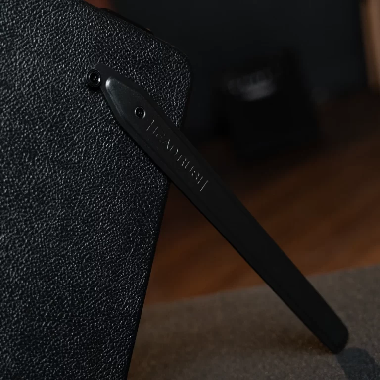 Close-up of a black textured carrying case with a black strap attached to its side, strap showing faint embossed text. Low lighting. ขายราคาพิเศษ
