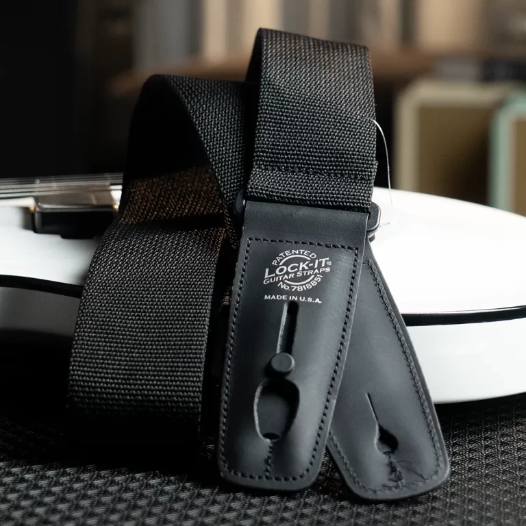 Black nylon guitar strap with leather end pieces and a patent logo, resting on a white guitar body ขายราคาพิเศษ