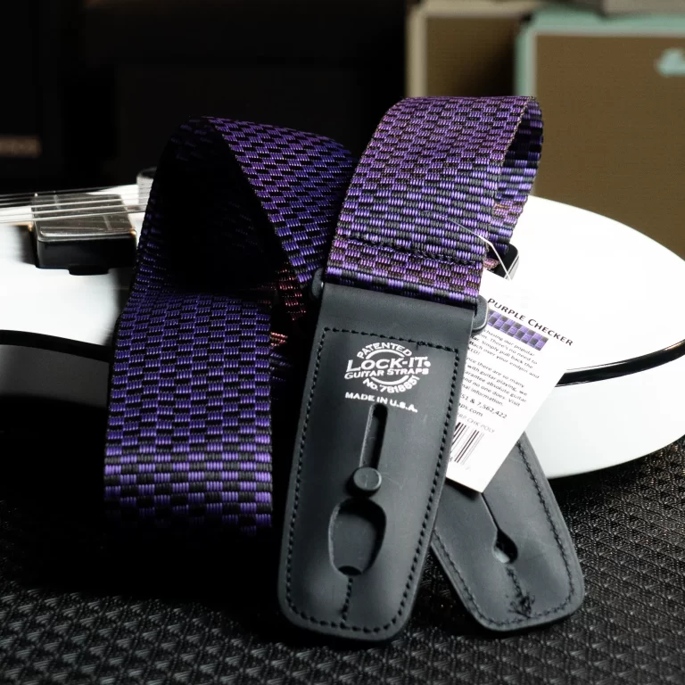 Close-up of a purple checkered guitar strap with black leather ends on a white surface, brochure nearby. ขายราคาพิเศษ