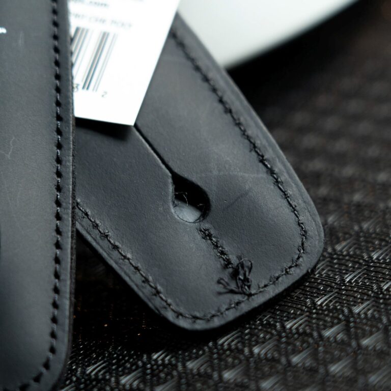 Close-up of a black leather strap with stitched seams and a punched hole, with a white tag tucked nearby. ขายราคาพิเศษ