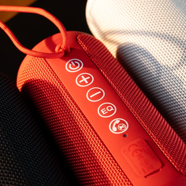 Close-up of a red portable speaker’s control panel with power, volume up, volume down, EQ, and call icons on a fabric strap edge. ขายราคาพิเศษ