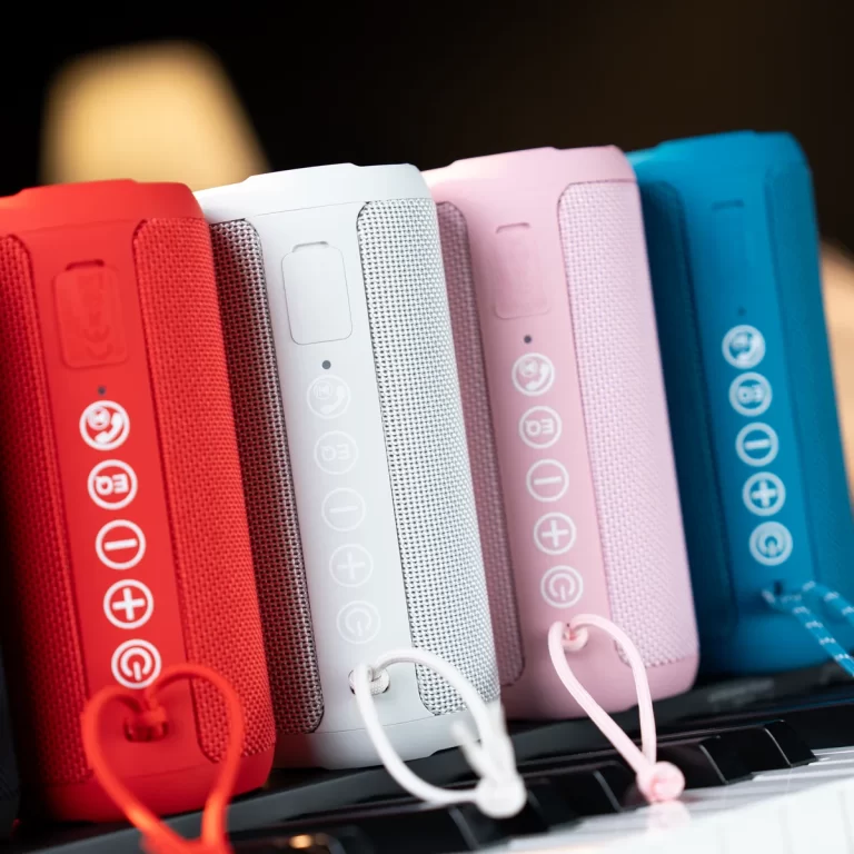 Row of colorful portable speakers in red, white, pink, and blue with cords hanging from a shelf. ขายราคาพิเศษ