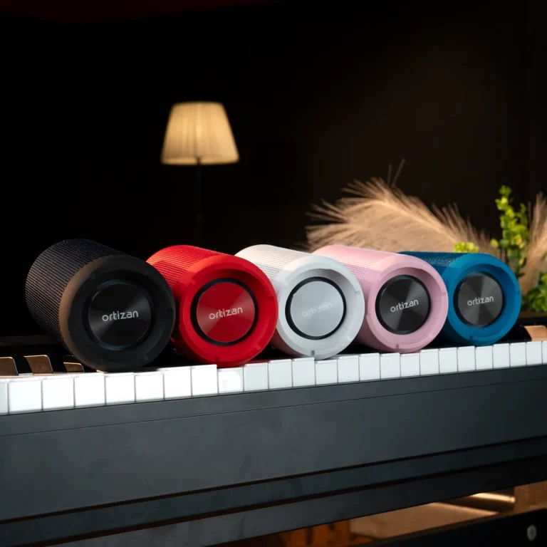 Six Ortizan portable speakers in black, red, white, pink, and blue lined up on a piano keyboard. ขายราคาพิเศษ