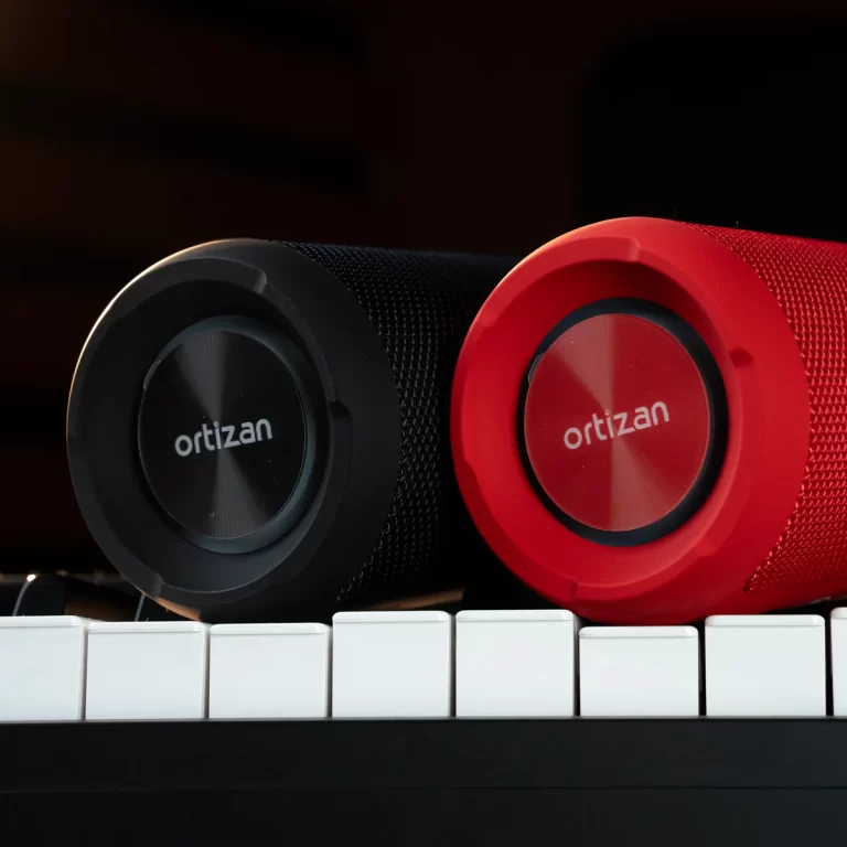 Two Ortizan portable speakers, one black and one red, rest on a white piano keyboard. ขายราคาพิเศษ