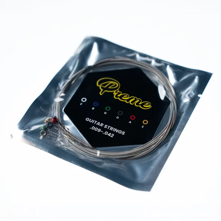 Guitar strings in a sealed foil package with a black card showing a yellow script logo and color‑coded markers for string gauges. ขายราคาพิเศษ