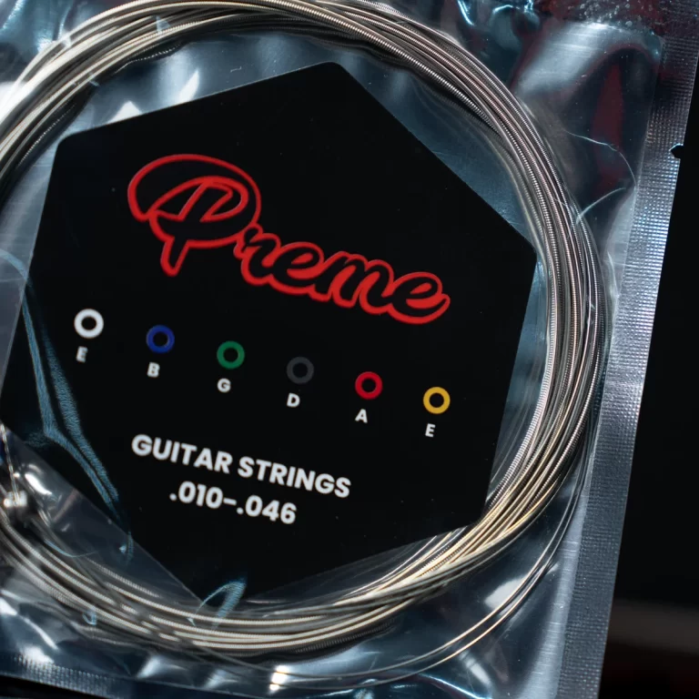 Coiled guitar strings in plastic packaging on a black card with the red 'Prime' logo and string notes E–E (E B G D A E) marked with colored dots on a guitar string set card. ขายราคาพิเศษ