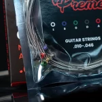 Plastic-wrapped guitar strings with color-coded ball ends partially visible, packaging shows 'GUITAR STRINGS' text ขายราคาพิเศษ