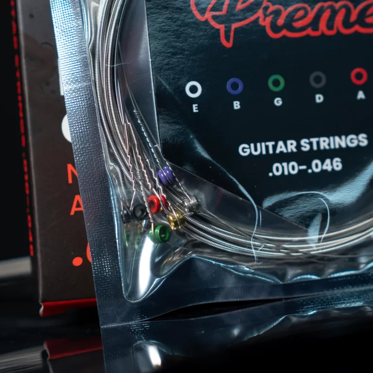Plastic-wrapped guitar strings with color-coded ball ends partially visible, packaging shows 'GUITAR STRINGS' text ขายราคาพิเศษ