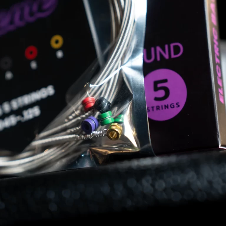 Close-up of jewelry components: silver cords with colorful bead tips inside a plastic bag near a purple '5 strings' label. ขายราคาพิเศษ