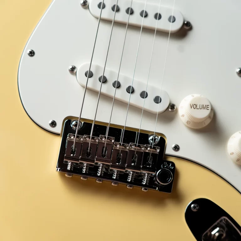 Close-up of a cream electric guitar showing the bridge, pickups, and six strings over a pale yellow body. ขายราคาพิเศษ