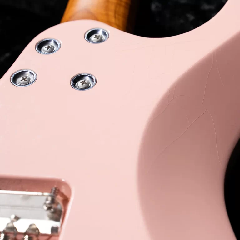 Close-up of a pink electric guitar body with four metal screws and a crackled finish in the paint. ขายราคาพิเศษ