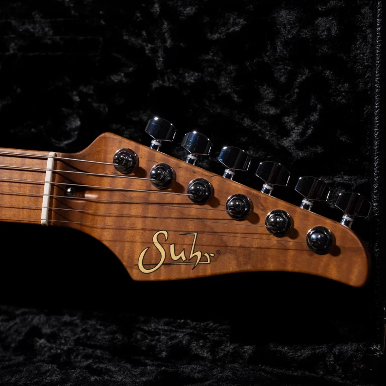 Close-up of a Suhr electric guitar headstock with six chrome tuners, strings, and the Suhr logo, resting in a black case lining. ขายราคาพิเศษ
