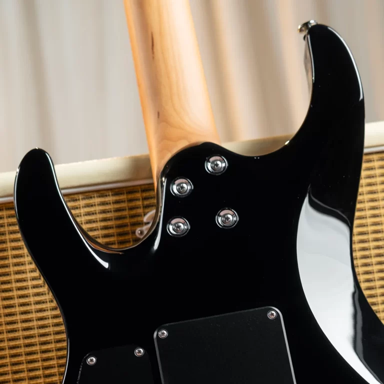 Back view of a black electric guitar with a natural wood neck, showing control knobs and back plates against a woven speaker cabinet. ขายราคาพิเศษ