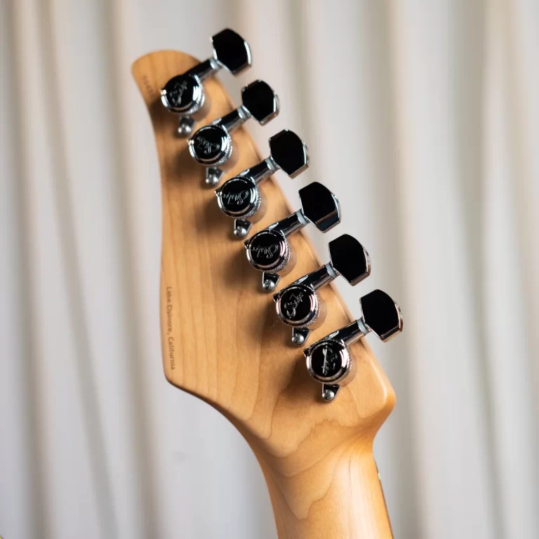Close-up of a wooden guitar headstock with six chrome tuning pegs and a blurred light backdrop ขายราคาพิเศษ