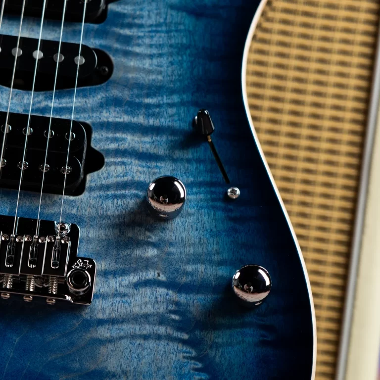 Close-up of a blue electric guitar body with chrome knobs, pickups, and metal bridge, shown with a woven amplifier in the background ขายราคาพิเศษ