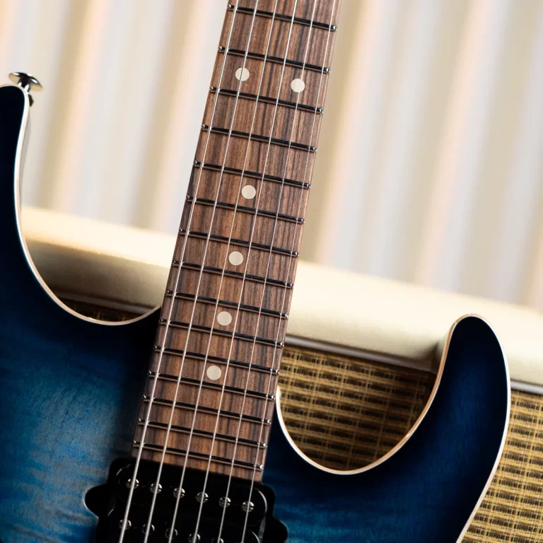 Close-up of a blue electric guitar neck and fretboard with metal frets and white dot inlays, against a blurred beige background. ขายราคาพิเศษ