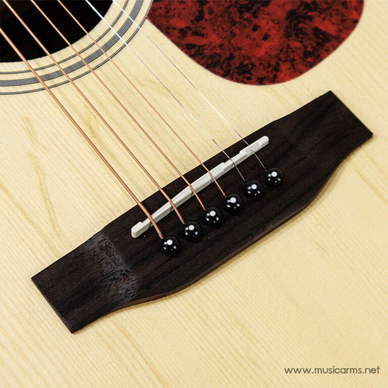Close-up of an acoustic guitar bridge with six strings anchored by black pins on a light wood body. ขายราคาพิเศษ