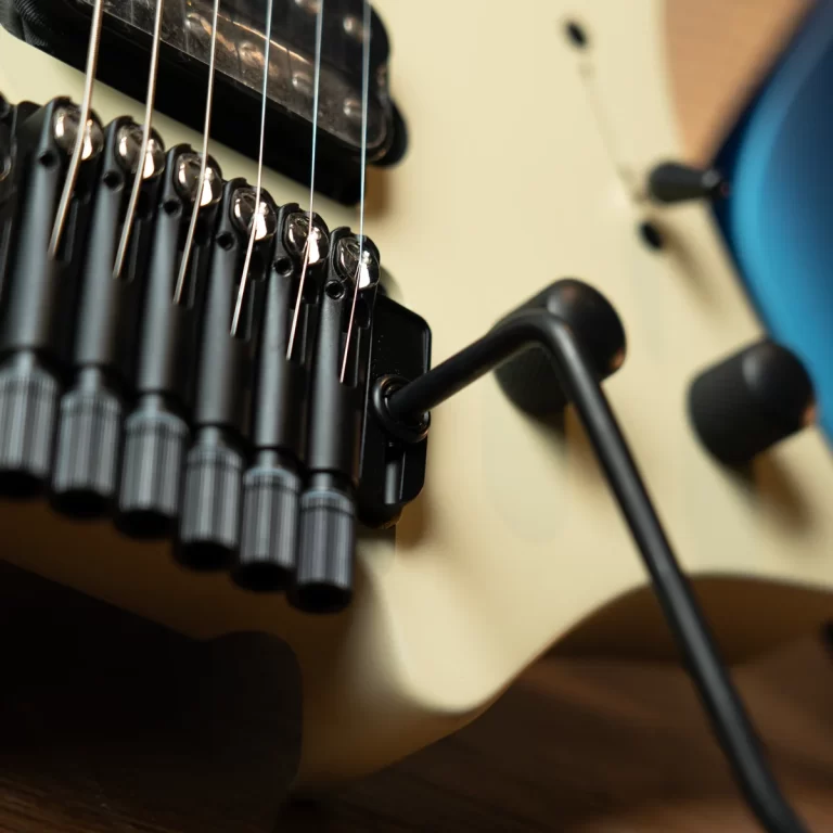 Close-up of an electric guitar's locking tremolo bridge with strings and a black tremolo arm on a cream body. ขายราคาพิเศษ