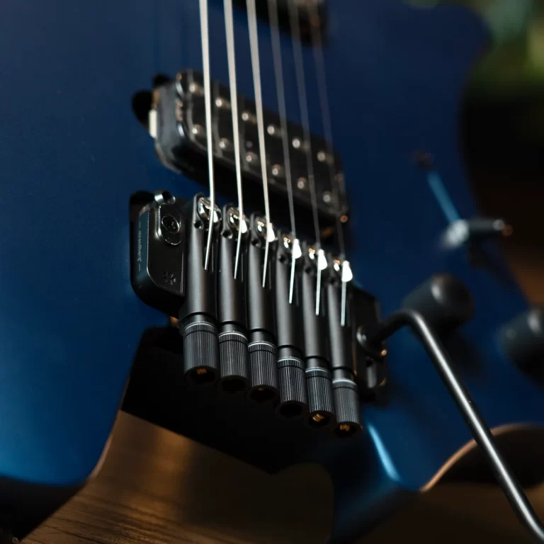 Close-up of a blue electric guitar bridge with multiple tremolo saddles and strings routed over them, showing tuning pegs and hardware detail ขายราคาพิเศษ