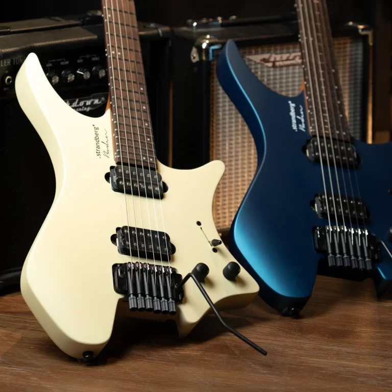 Two electric guitars resting on a wooden floor, a white Strat-style (with tremolo) on the left and a blue guitar on the right, with amplifiers in the background. ขายราคาพิเศษ