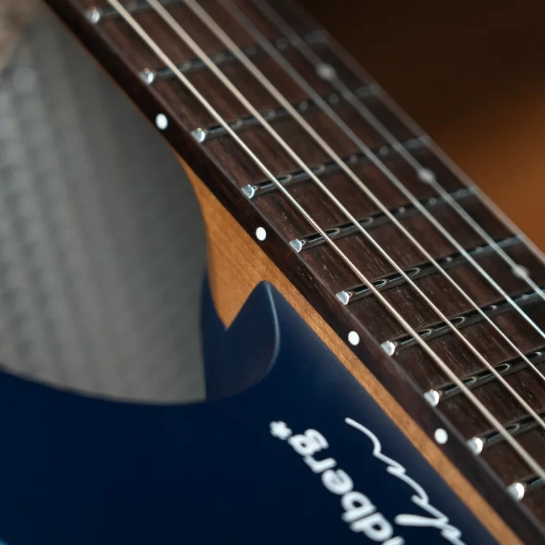 Close-up of a guitar neck showing metal frets and strings on a dark wood fretboard, with a blue body in the foreground. ขายราคาพิเศษ
