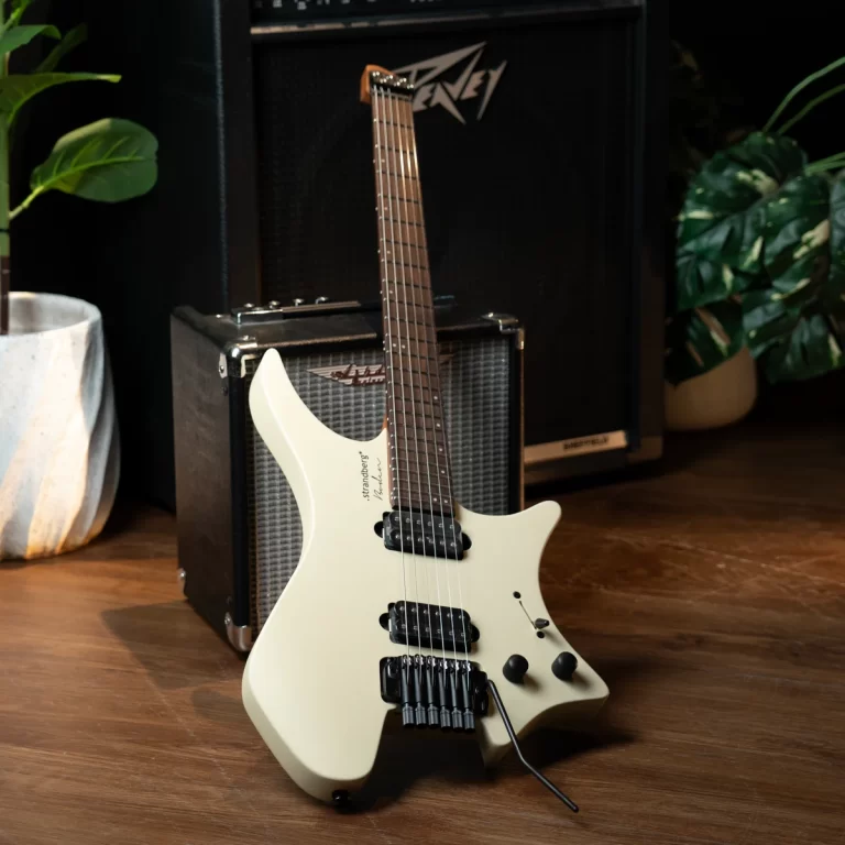 White electric guitar on a wooden floor in front of a guitar amplifier, with green plants nearby. ขายราคาพิเศษ